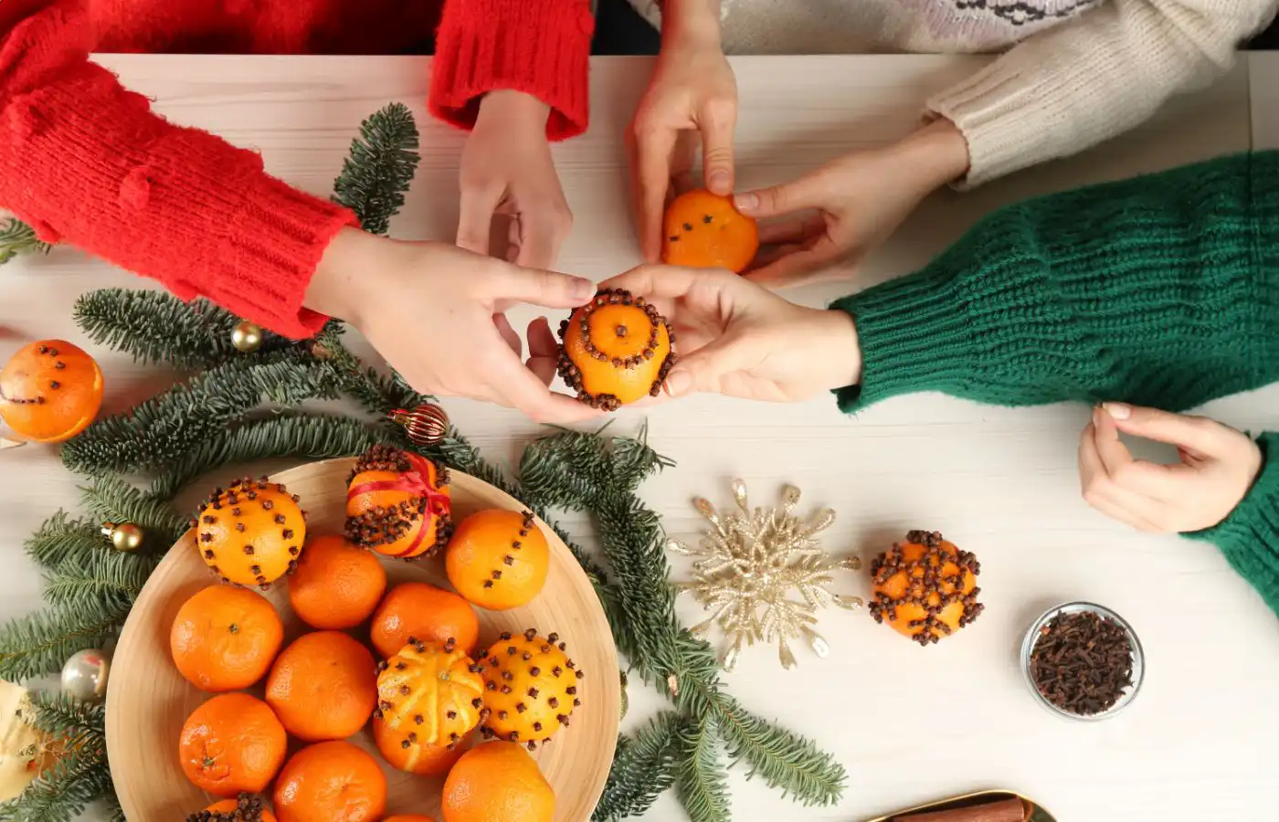 DIY de Noël : oranges piquées de clous de girofle entourées de branches de sapin, créant une décoration naturelle et parfumée pour les fêtes.