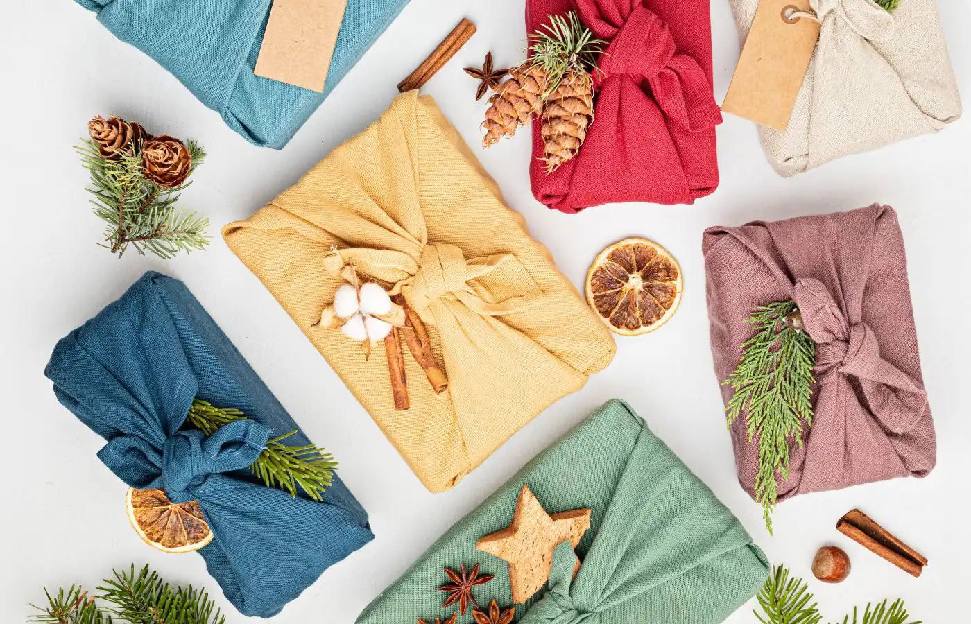 Emballages cadeaux éco-responsables en tissu avec des décorations naturelles comme des branches de sapin, des oranges séchées et des bâtons de cannelle pour un Noël durable.