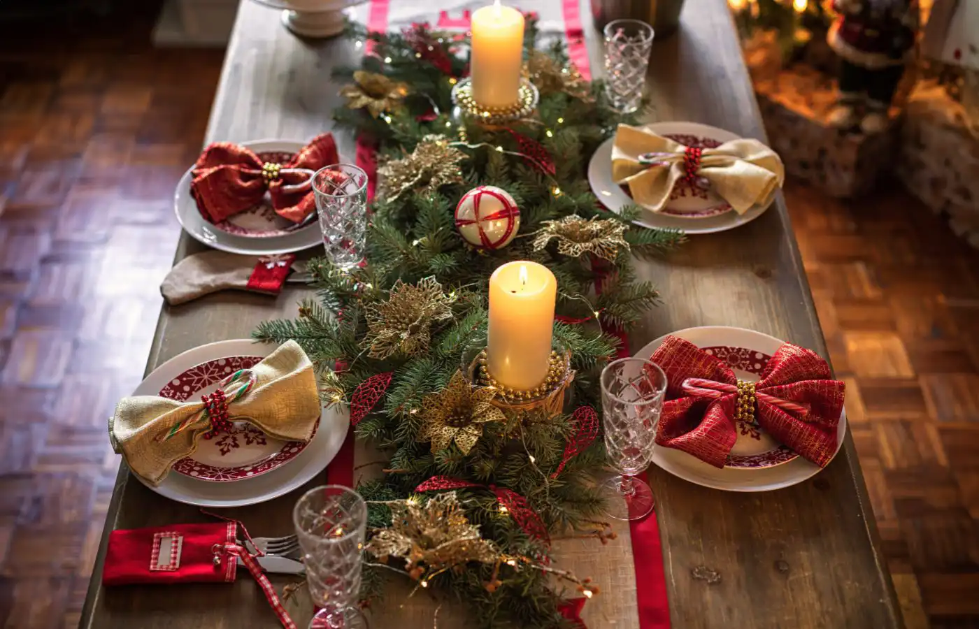 Table de Noël décorée avec des bougies, des branches de sapin et des accents dorés et rouges, créant une ambiance festive et chaleureuse.